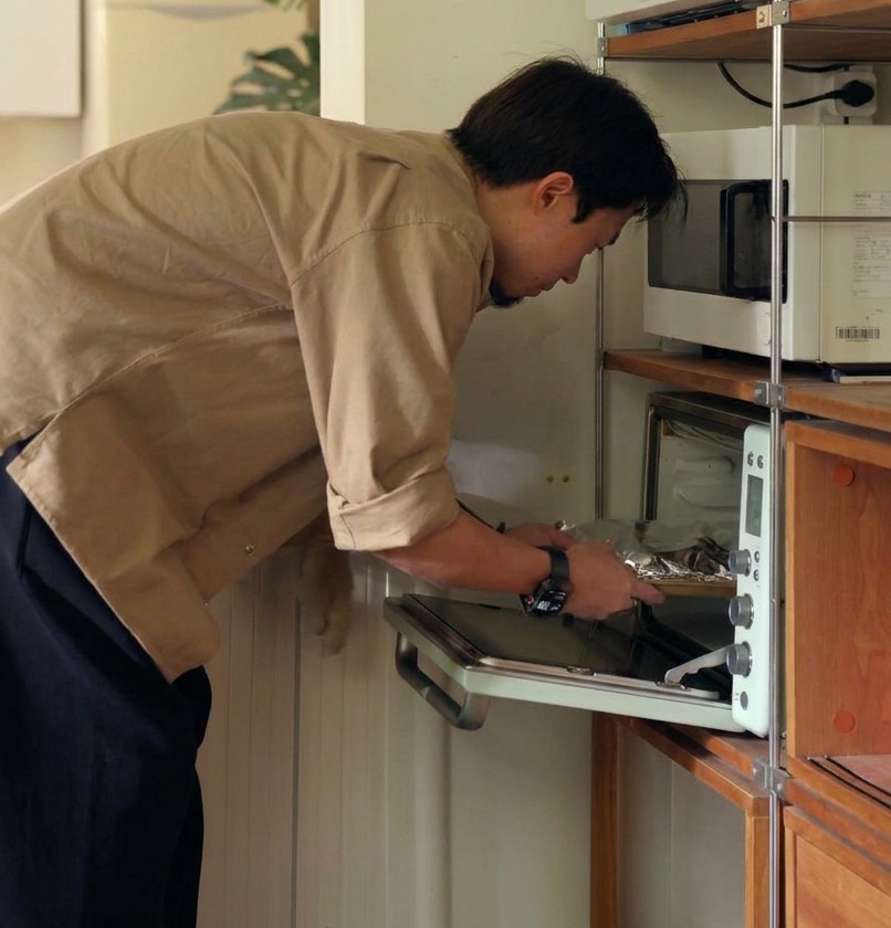 A person placing a tray of ribs wrapped tightly in aluminum foil into a small white countertop oven for slow baking.