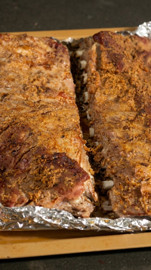 Two racks of cooked pork ribs resting on a baking tray with the aluminum foil opened up to expose the meat.
