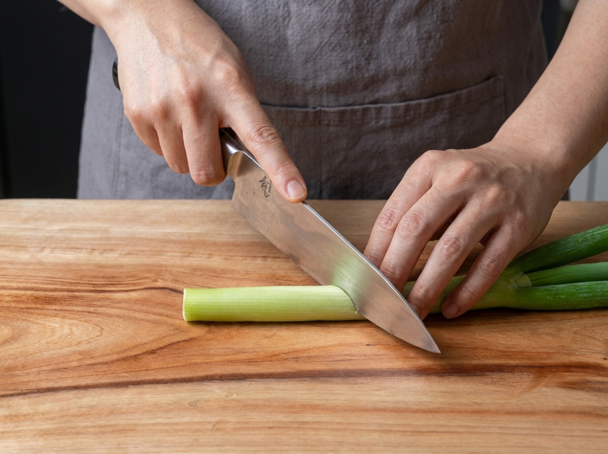 Fresh green onions being sliced into small, uniform pieces on a wooden board.