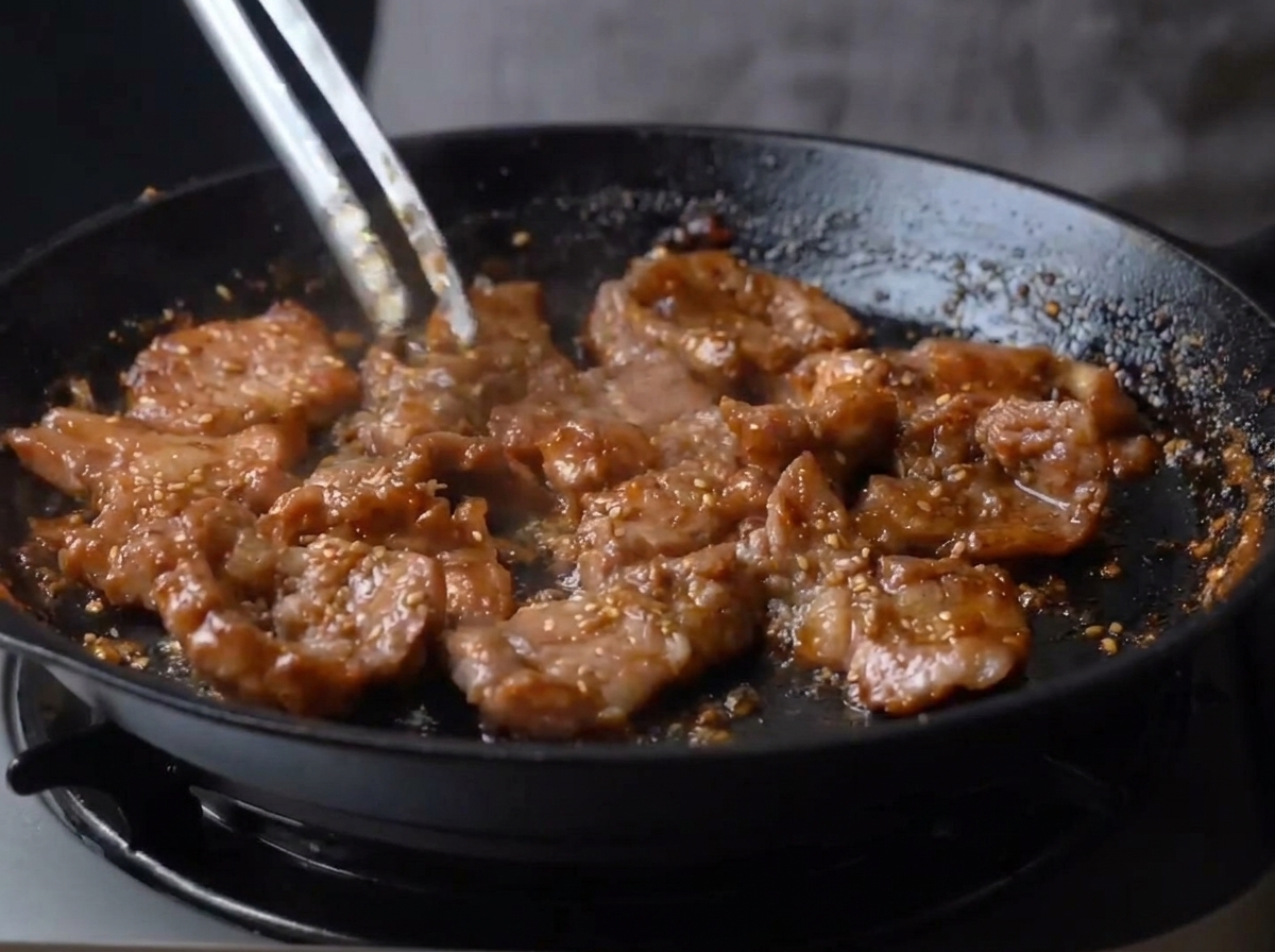 Bite-sized pieces of pork being stirred in a skillet, coated in a thick, shiny, dark brown caramelized glaze.