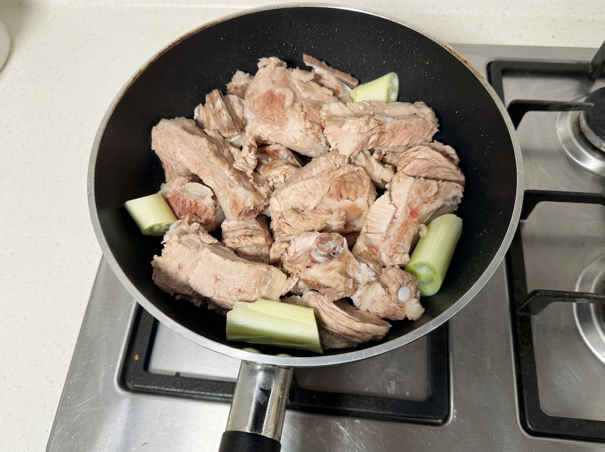Raw pork ribs and scallion segments resting in a black pan.