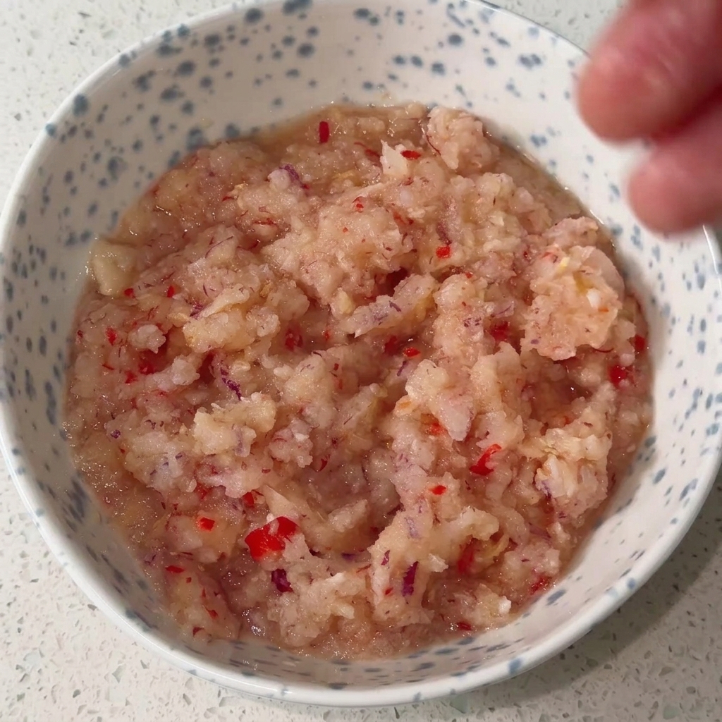 A bowl containing a blended onion and chili base being mixed with various liquid and powder seasonings to create a rich red sauce.