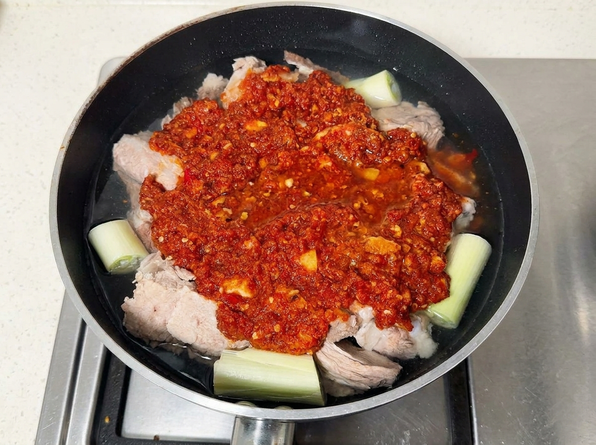 Pork ribs topped with red chili paste sitting in a pan filled with water.