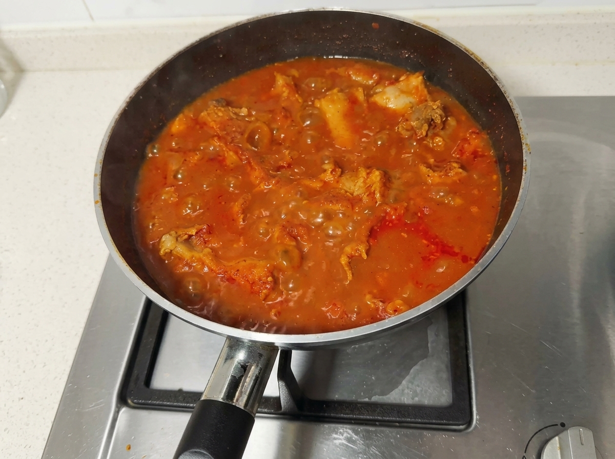 Spicy red pork rib stew bubbling vigorously in a pan on the stovetop.