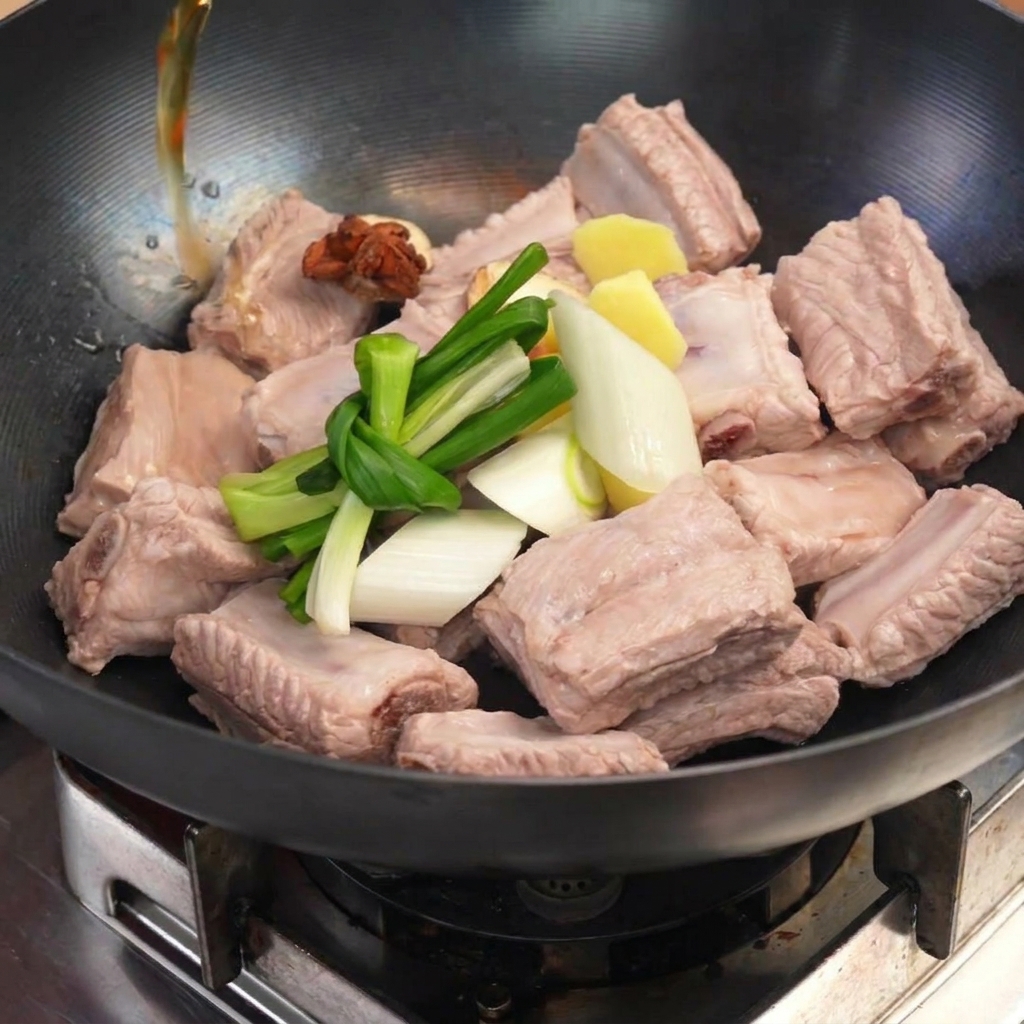 Parboiled ribs in a wok topped with knotted green onions, ginger, and star anise as liquid is poured in.