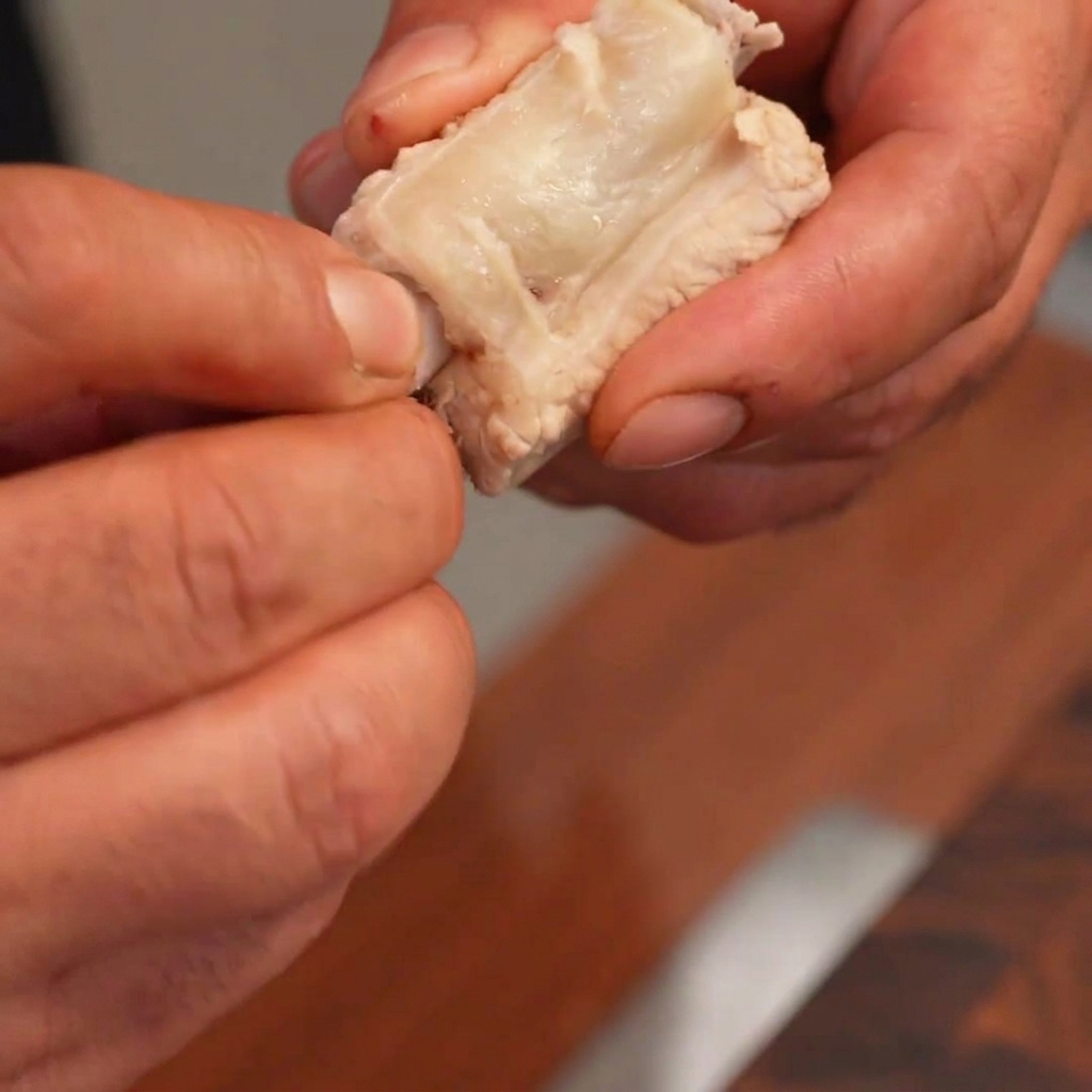 Hands carefully removing a bone from a piece of cooked pork rib and stuffing it with a cylindrical white rice cake.