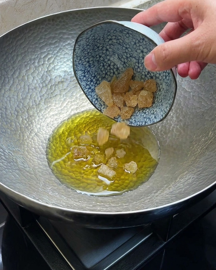 Rock sugar melting and caramelizing in hot oil within a metal wok.