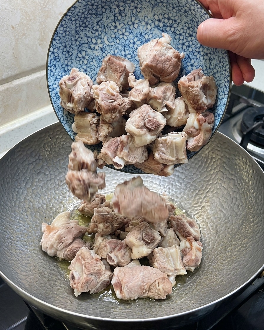 Pork ribs being stirred in a wok with ginger, star anise, and dried chili.