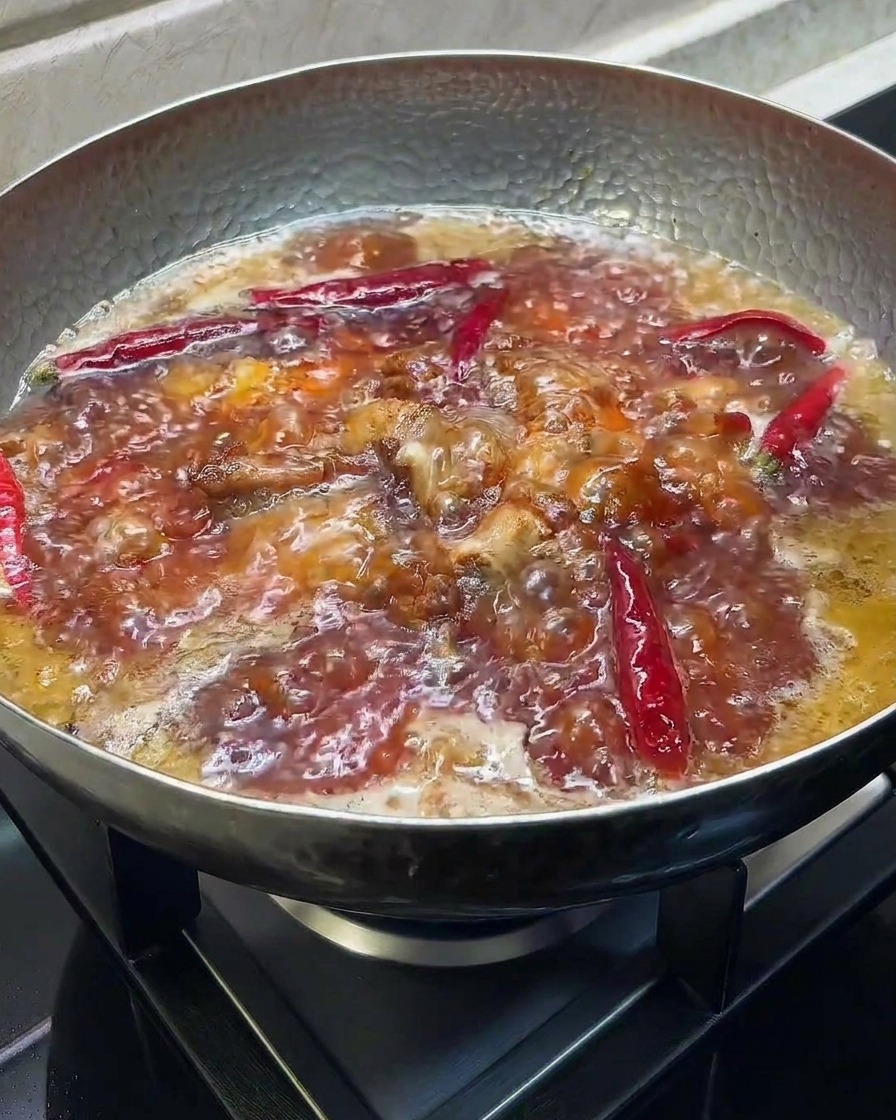 Dark soy sauce and vinegar being added to a bubbling pot of braised ribs.