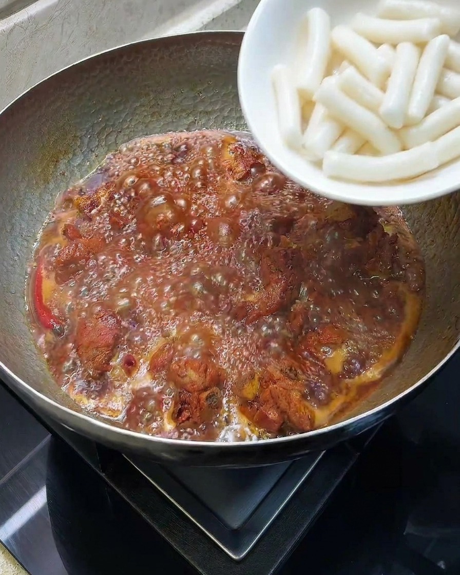 White cylindrical rice cakes being dropped into a pot with simmering braised ribs.