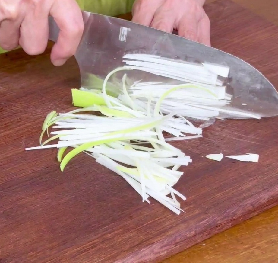 Finely sliced green onion strips on a wooden cutting board, ready for the marinade.