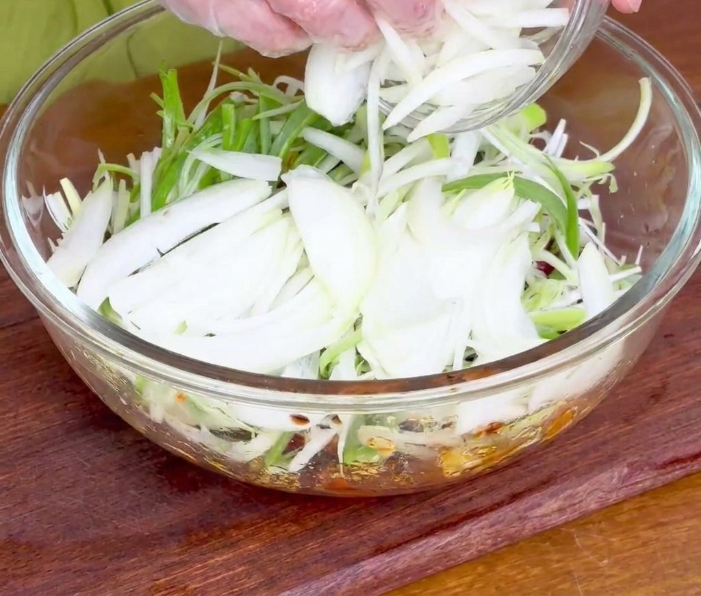 Hands adding a handful of sliced white and green onions to the marinating raw beef.