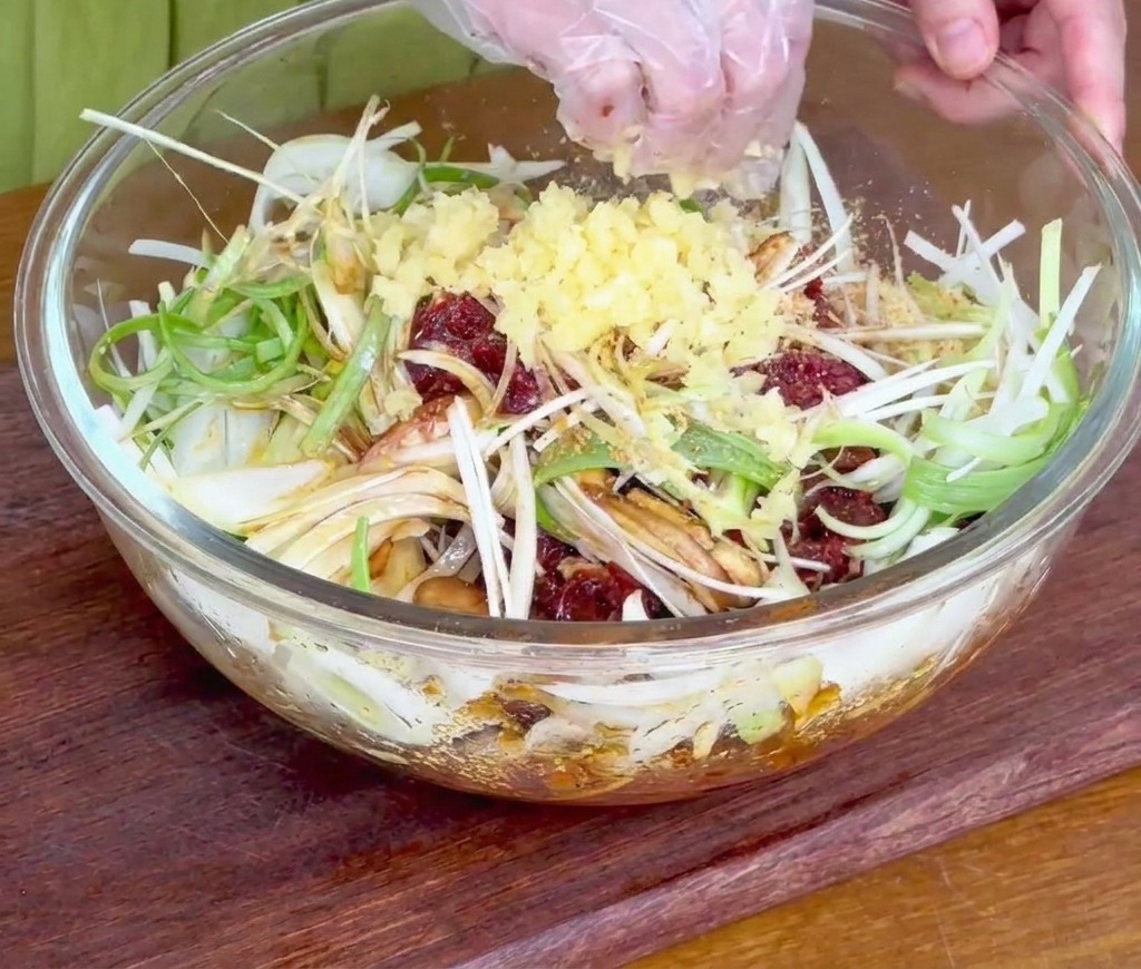 A hand sprinkling freshly minced garlic over the beef and sliced onions in a glass mixing bowl.