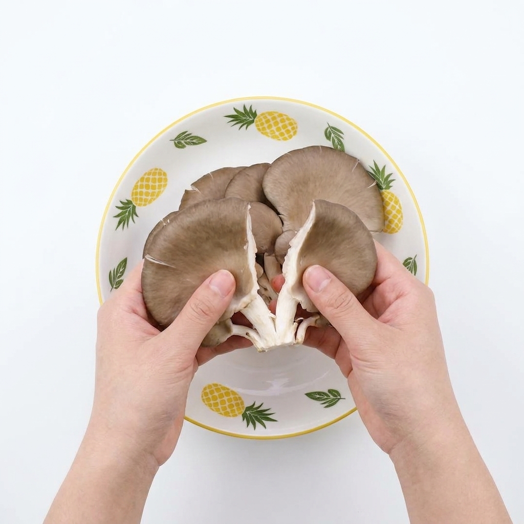 Hands tearing raw oyster mushrooms into smaller strips over a patterned bowl.