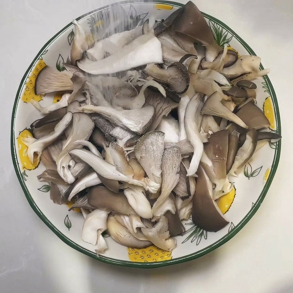 A bowl filled with torn raw oyster mushrooms being sprinkled with salt.