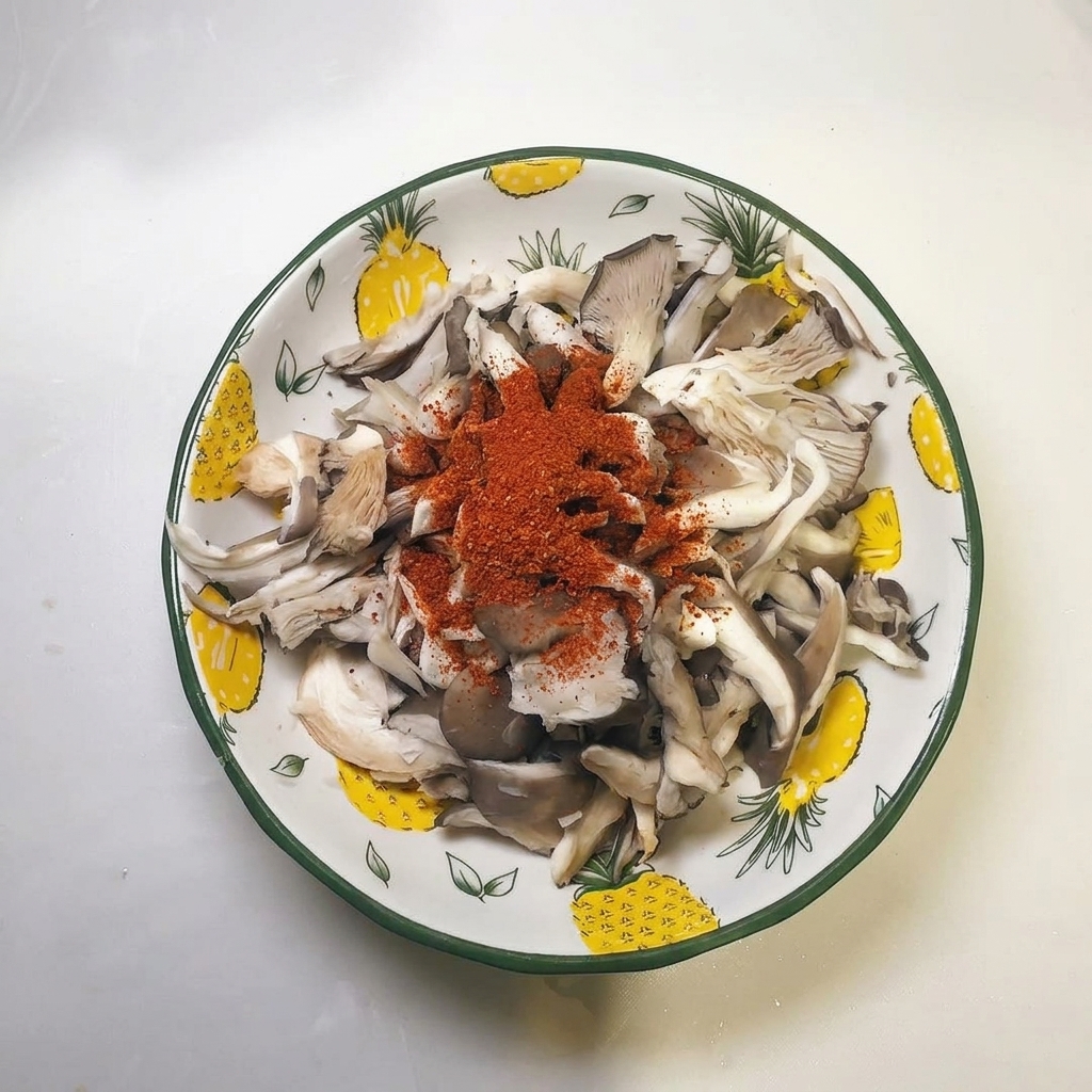 A pile of red chili powder sitting on top of the squeezed oyster mushroom strips in a bowl.