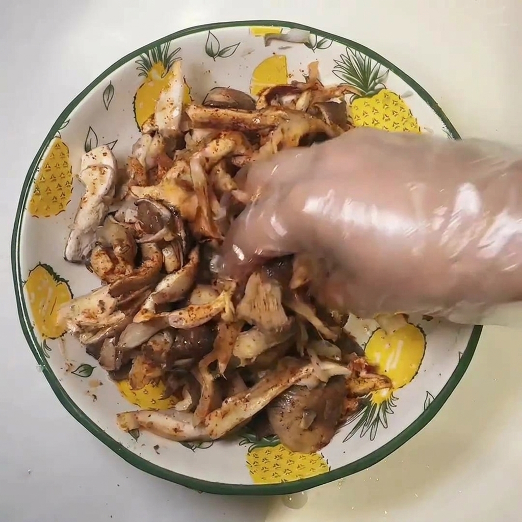 A hand in a plastic glove mixing seasoned mushrooms in a bowl.