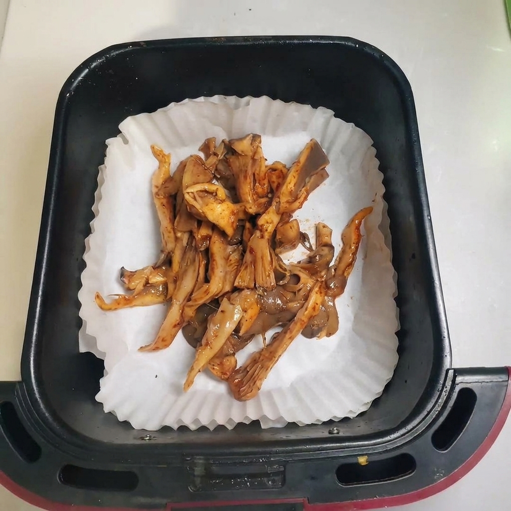 Seasoned mushrooms spread out in an air fryer basket lined with parchment paper.