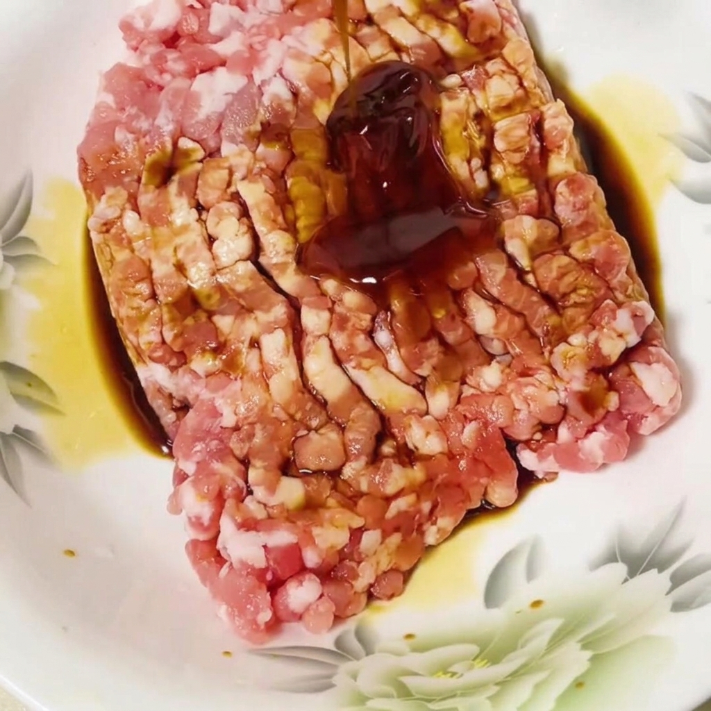 Oyster sauce added to the seasoned minced pork in a bowl.