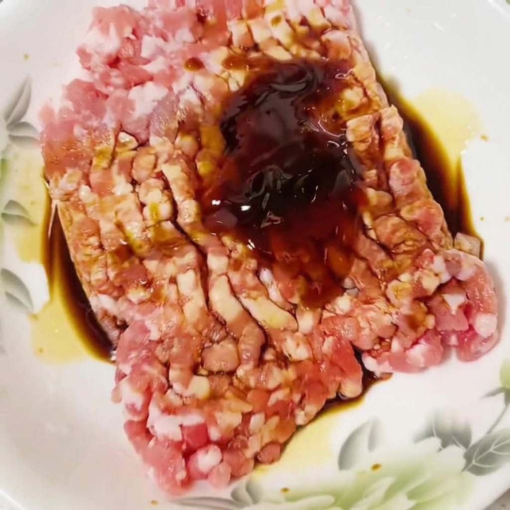Chicken essence being sprinkled over the raw meat mixture.