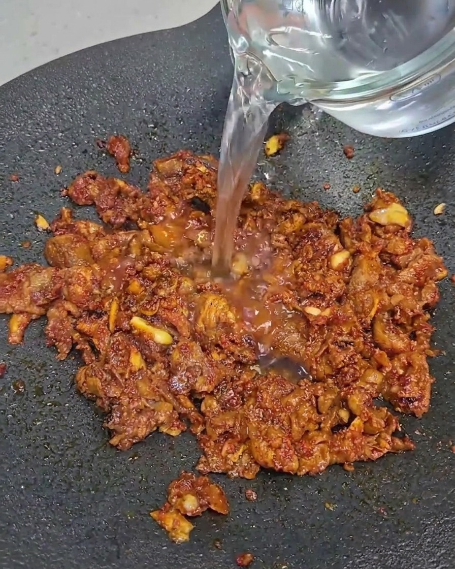 Slices of beef belly cooking in a black pan.