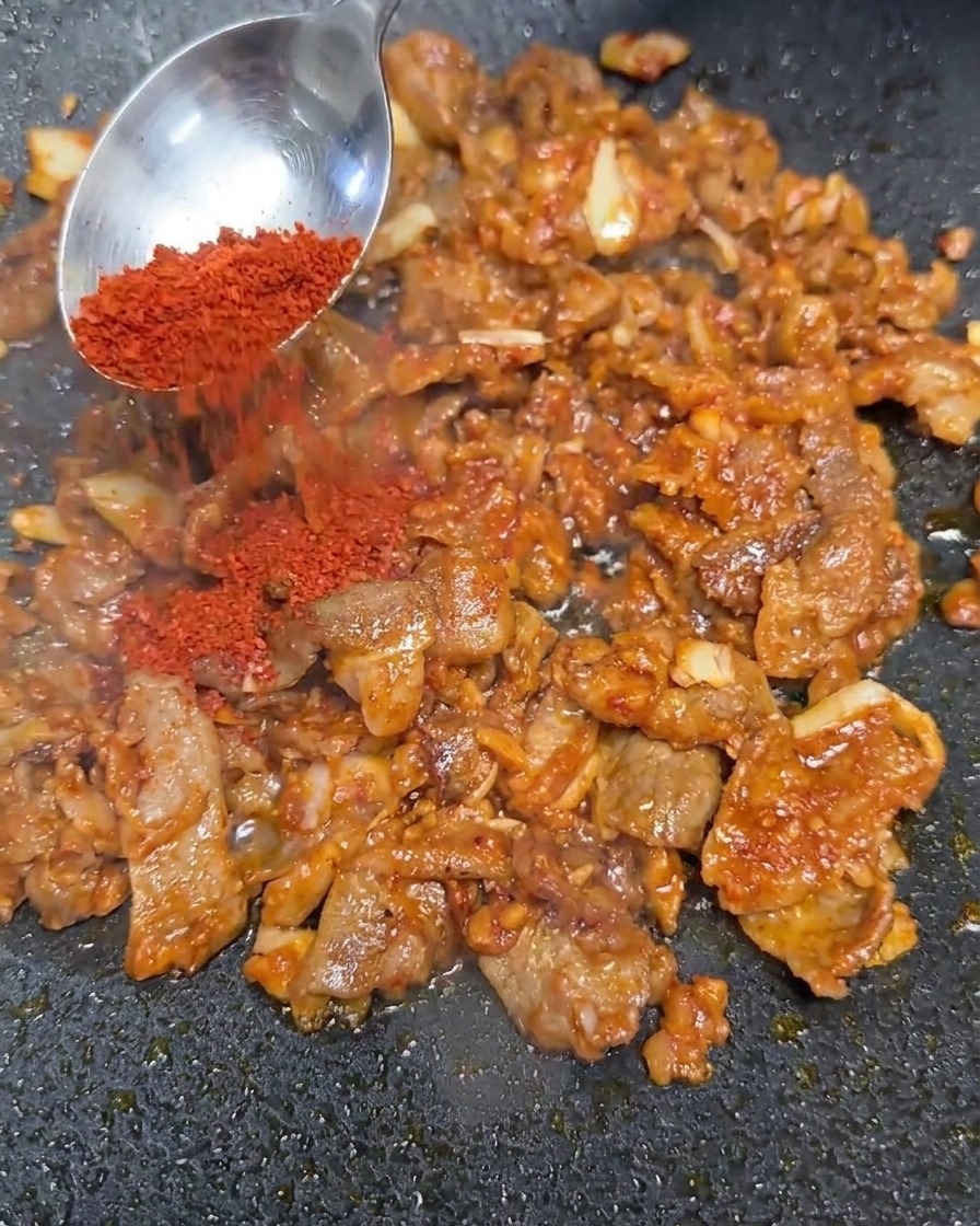 Red chili powder being added to the stir-fried beef mixture.
