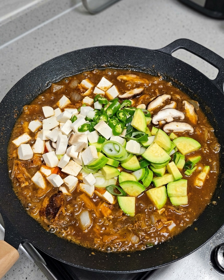 Vegetables and tofu being added to the simmering stew.