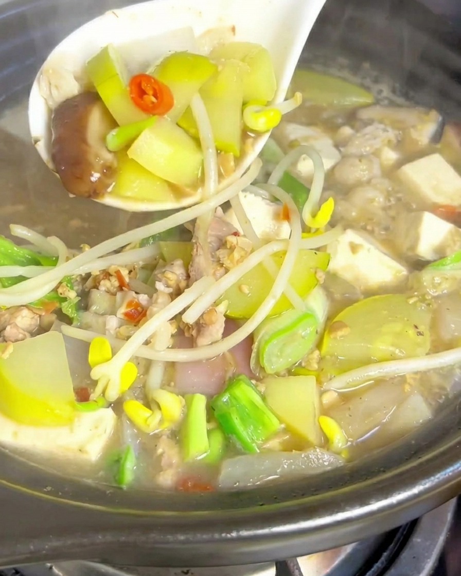 Clear water being poured into a clay pot with browned pork slices at the bottom.