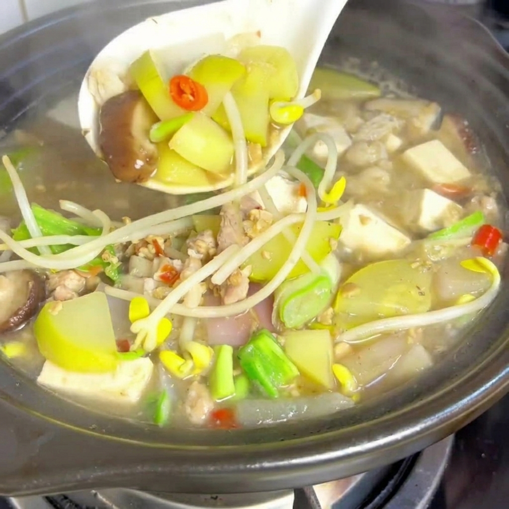 Soft tofu cubes being placed into the pot of simmering stew.