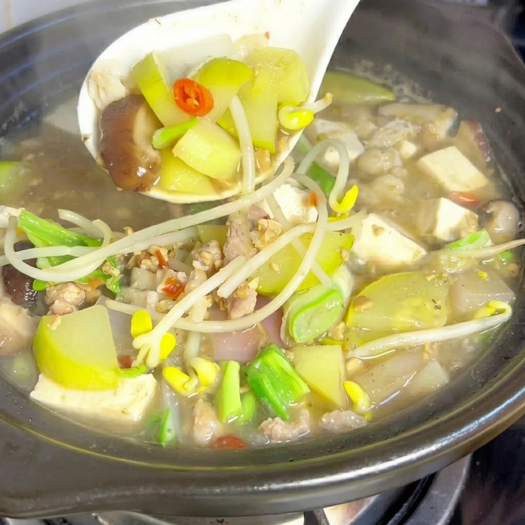 A metal spoon mixing a large dollop of fermented soybean paste into the bubbling stew broth.
