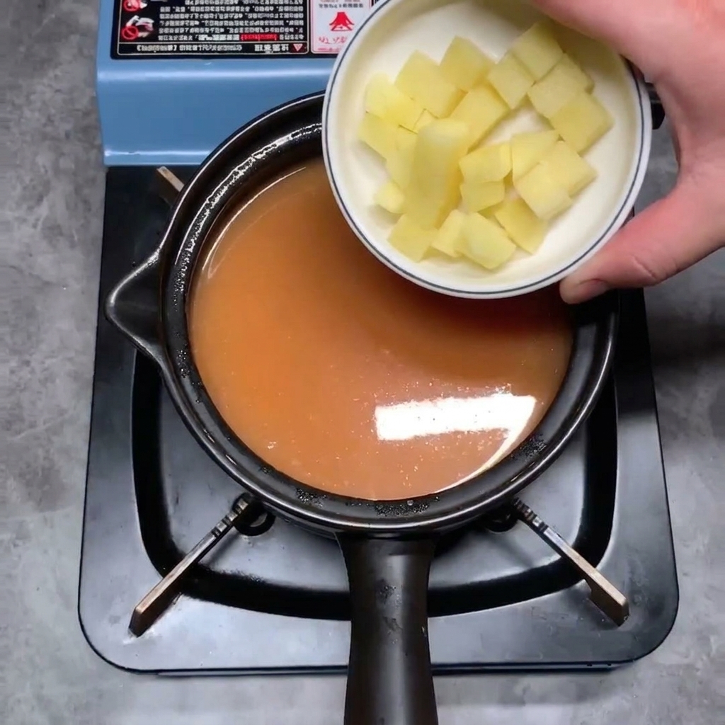 Diced raw potato cubes being dropped into the simmering orange-colored stew base.