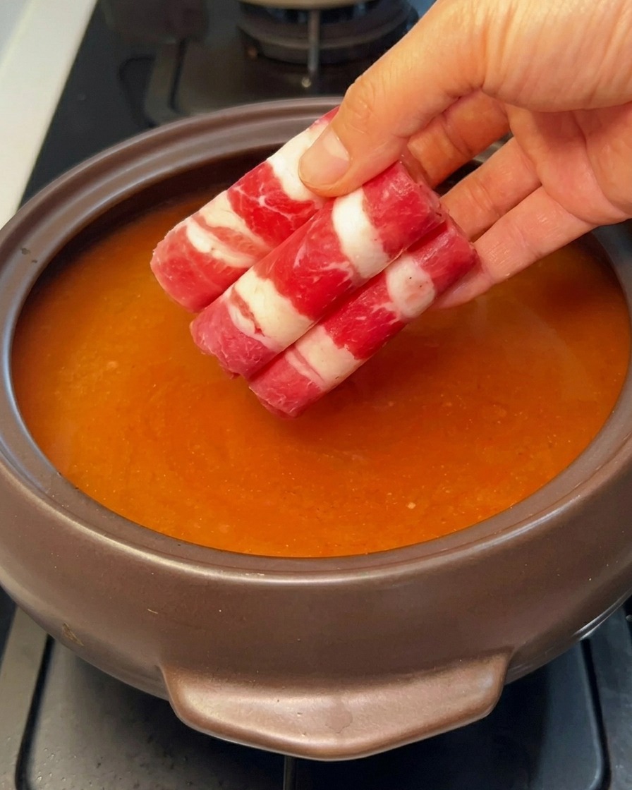 Thinly sliced, rolled fatty beef being added to the simmering red broth.