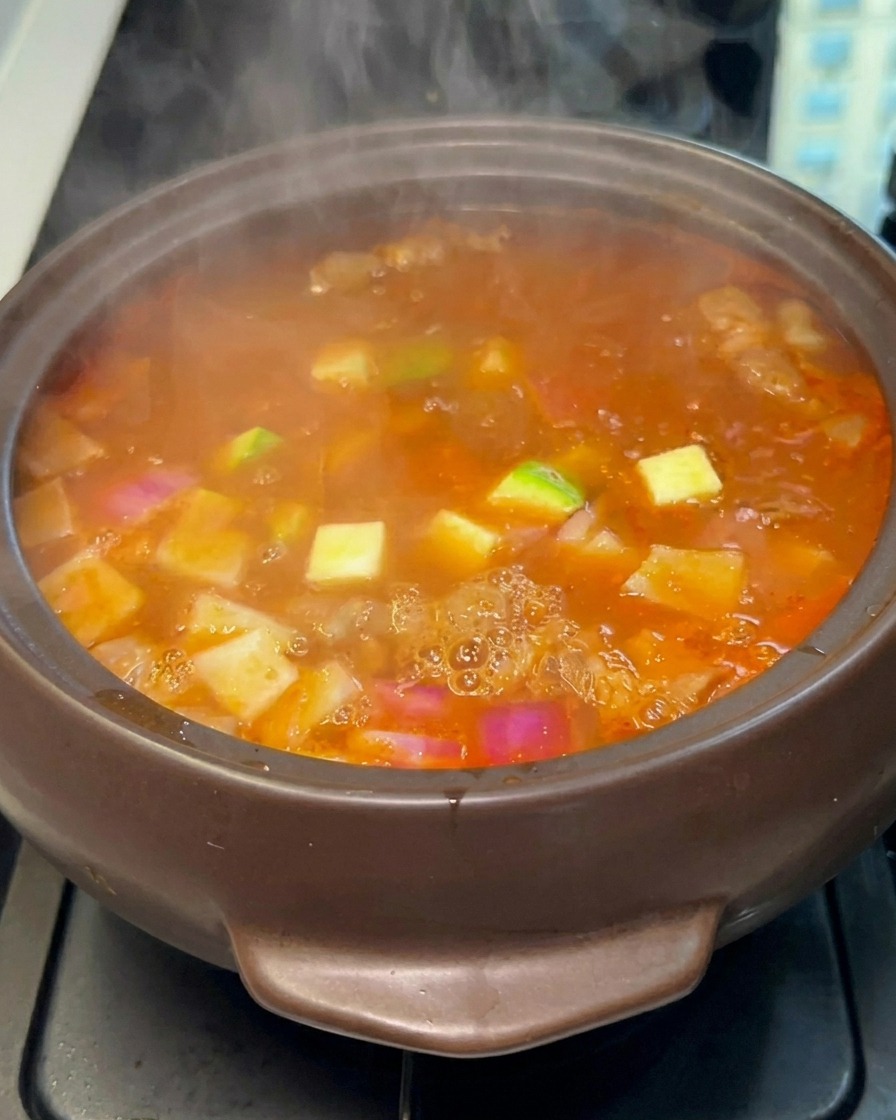 Diced green zucchini being added to the colorful stew pot.
