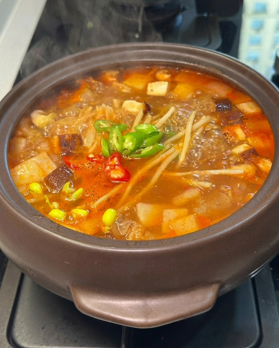 Sliced red and green chili peppers scattered over the simmering vegetables in a spicy red broth.