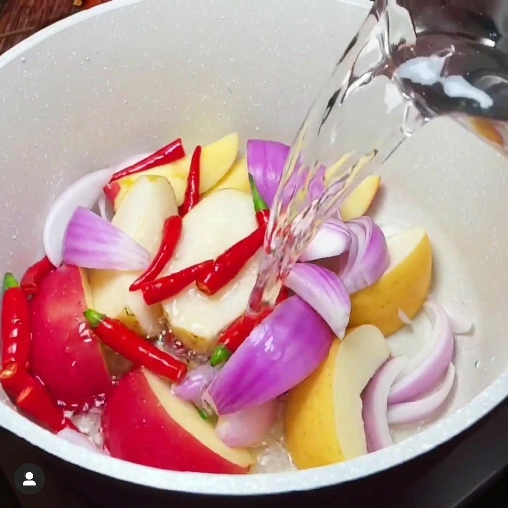 Liquid seasonings being poured into a white pot containing a mixture of chopped fruits and vegetables.