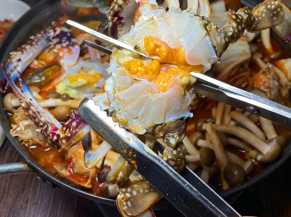 A cleaned raw crab being halved and added to the simmering stew pot.