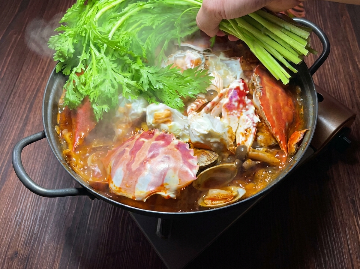 Fresh crown daisy greens and green onions being added as a garnish to the finished crab and kimchi stew.