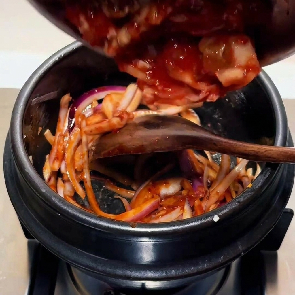 Chopped kimchi being added to the pot with the stir-fried onion and sauce base.