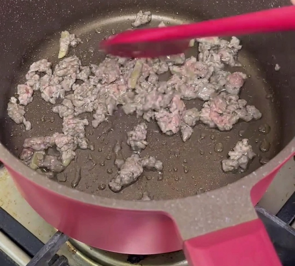 Minced beef being stir-fried with ginger slices in a pan until browned.