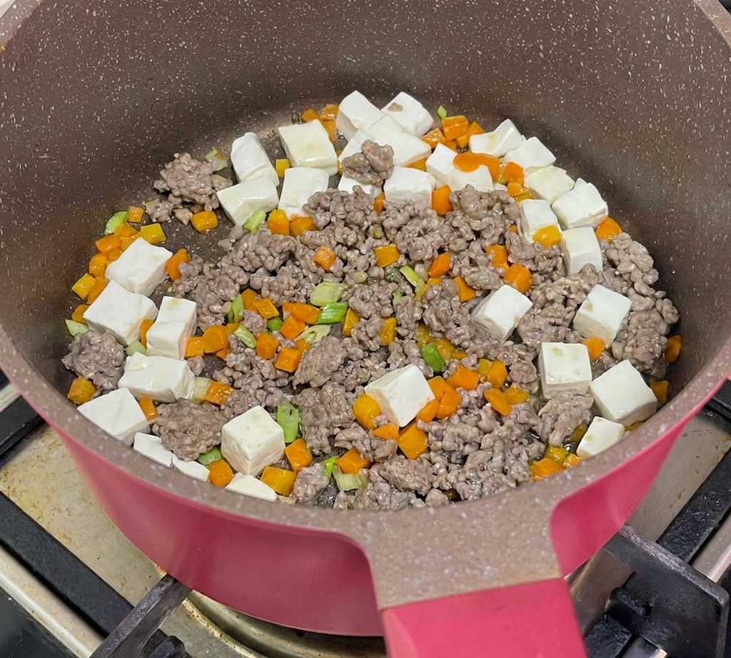 Hot water being poured into the pan containing tofu, beef, and carrots to simmer.