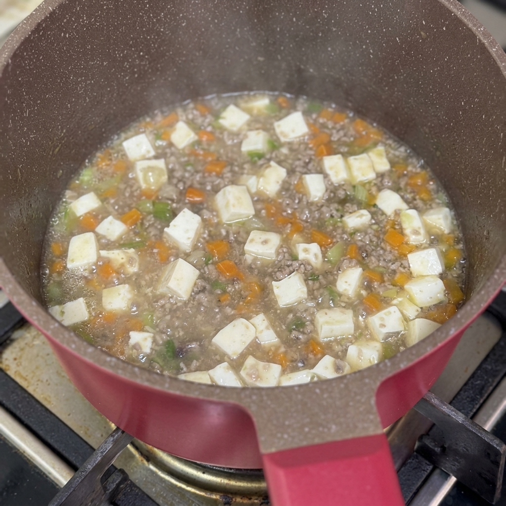 Cornstarch slurry being poured into the pan of simmering beef and tofu stew.