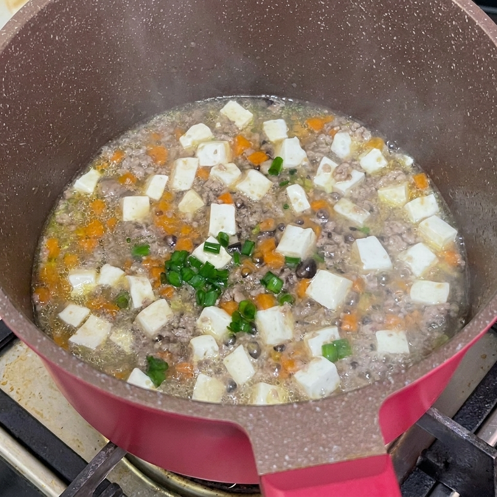 Freshly chopped green scallions being sprinkled over the finished beef and tofu stew in the pan.