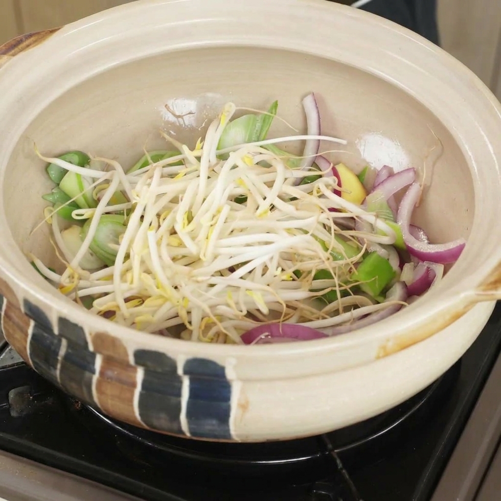Fresh bean sprouts added on top of sautéed onions and aromatics in a clay pot.