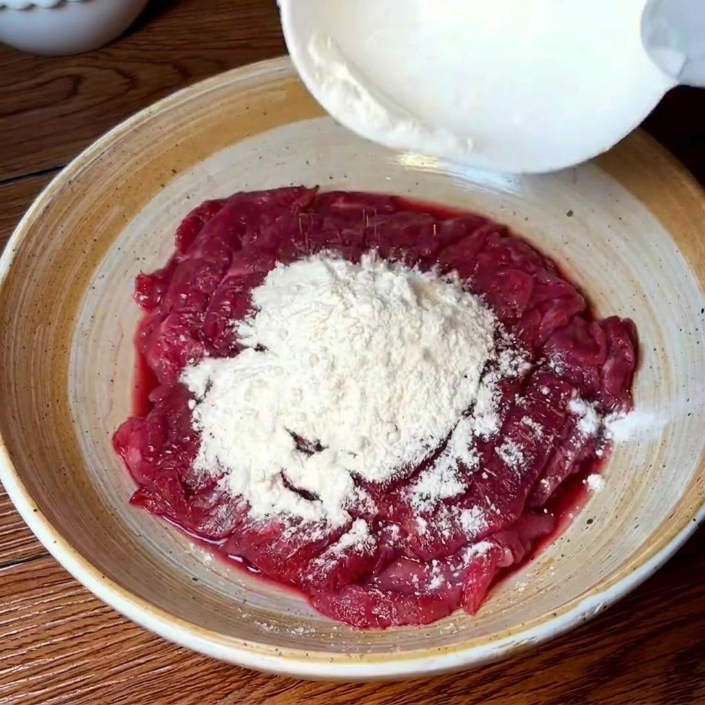 Beef slices being massaged in a bowl with water and flour to remove impurities.