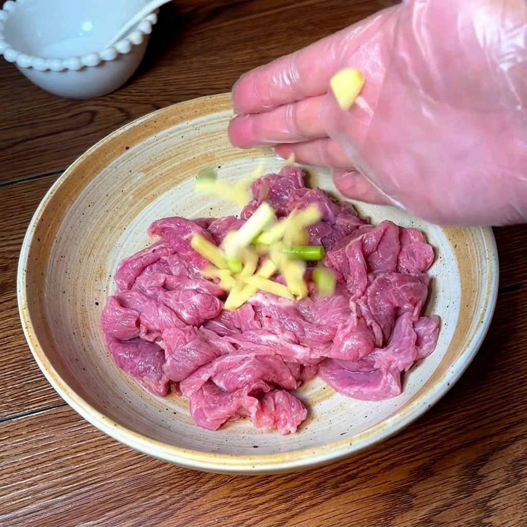 Hand in a clear glove seasoning and massaging beef slices with aromatics and spices.