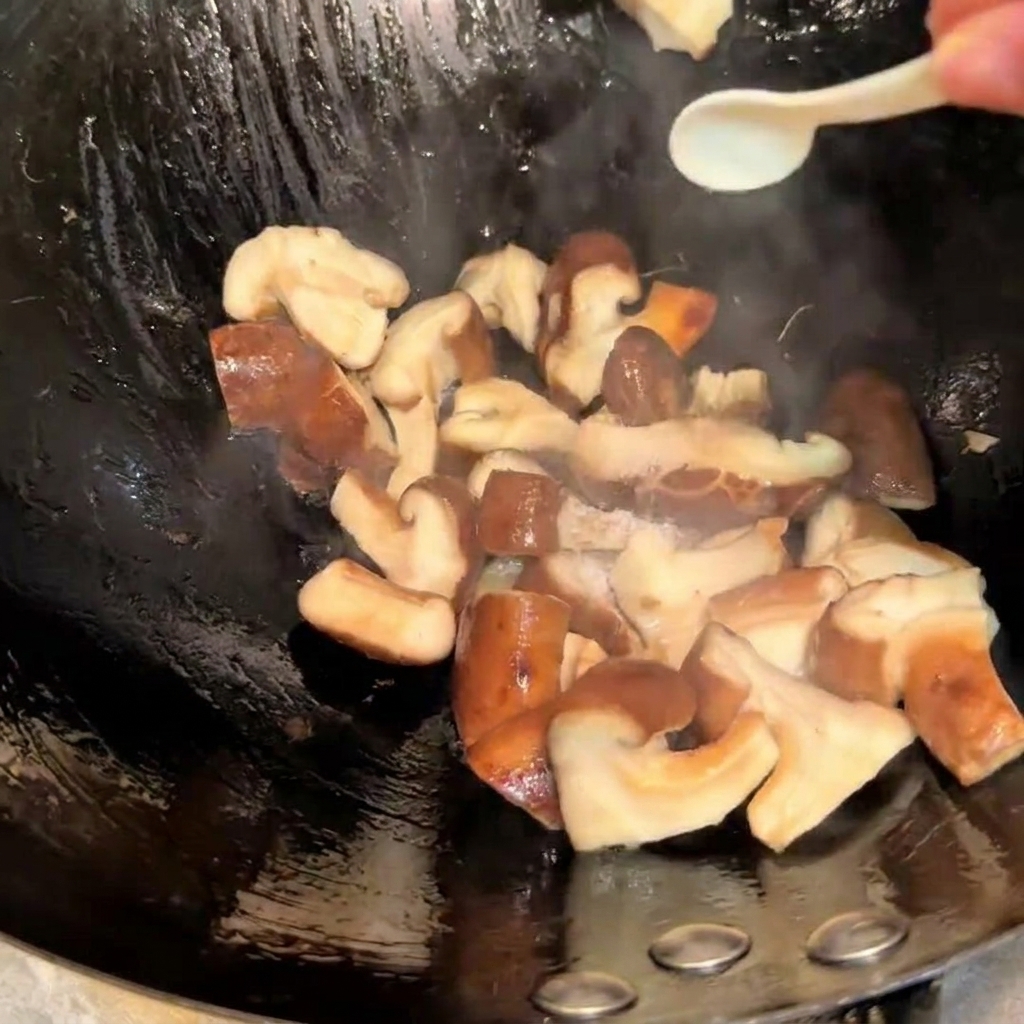 Seasoning the stir-frying shiitake mushrooms in a wok with salt and soy sauce using a small spoon.