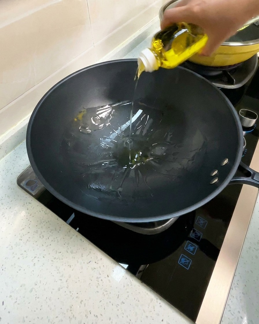 Cooking oil being poured into a preheated black wok.