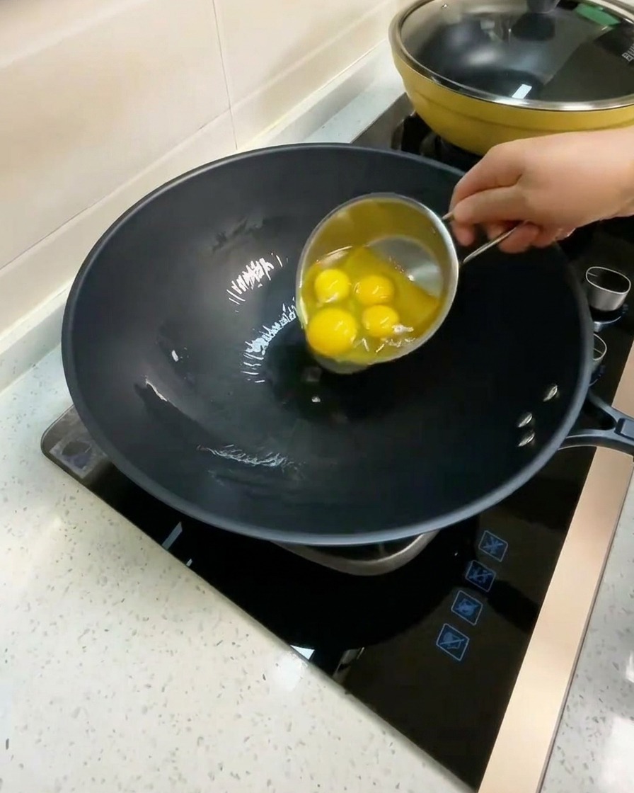 Four raw eggs being cracked into a wok with hot oil.