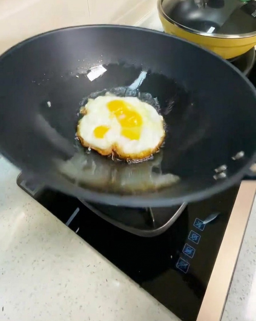 Fried egg being flipped in a hot wok, showing a golden brown underside.