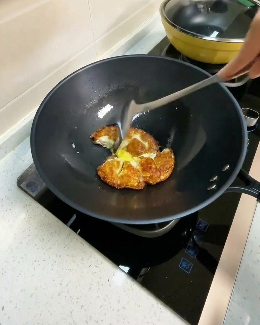 Hot water being poured into a wok containing fried egg pieces.